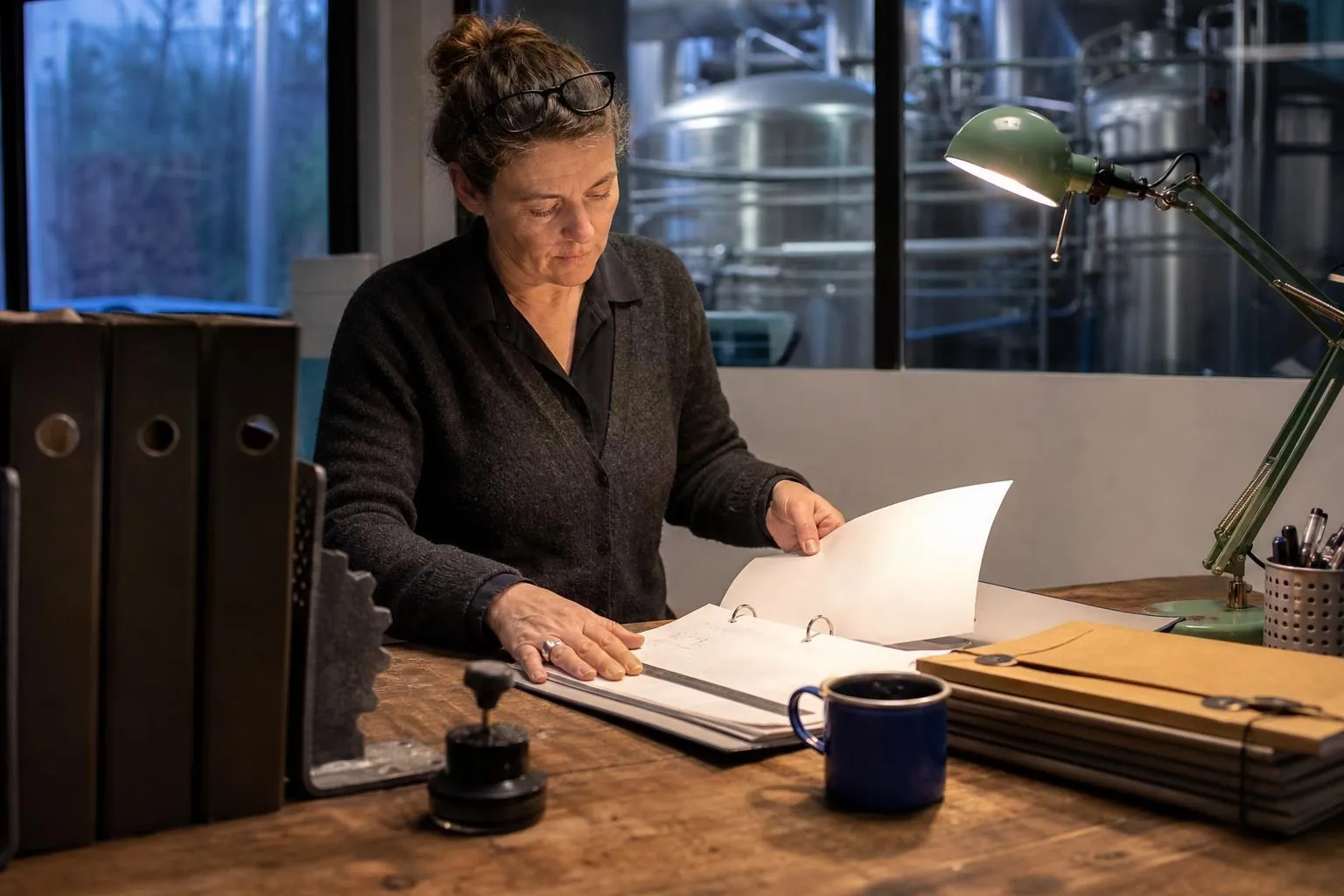 Une responsable de brasserie feuillette un classeur à levier sur un bureau installé dans un angle de l’atelier